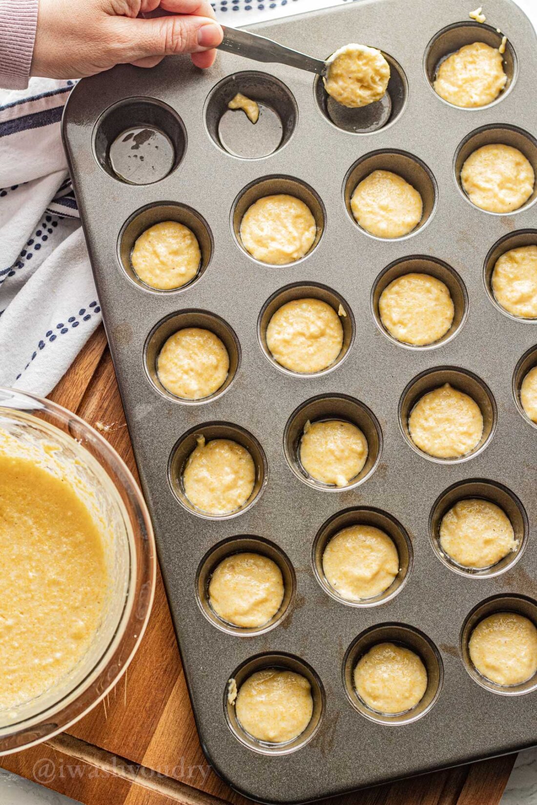 spooning corn batter into muffin pan with spoon.
