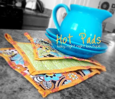 3 hot pads next to a blue pitcher on two blue plates and titled, " Hot Pads, baby night night boutique"