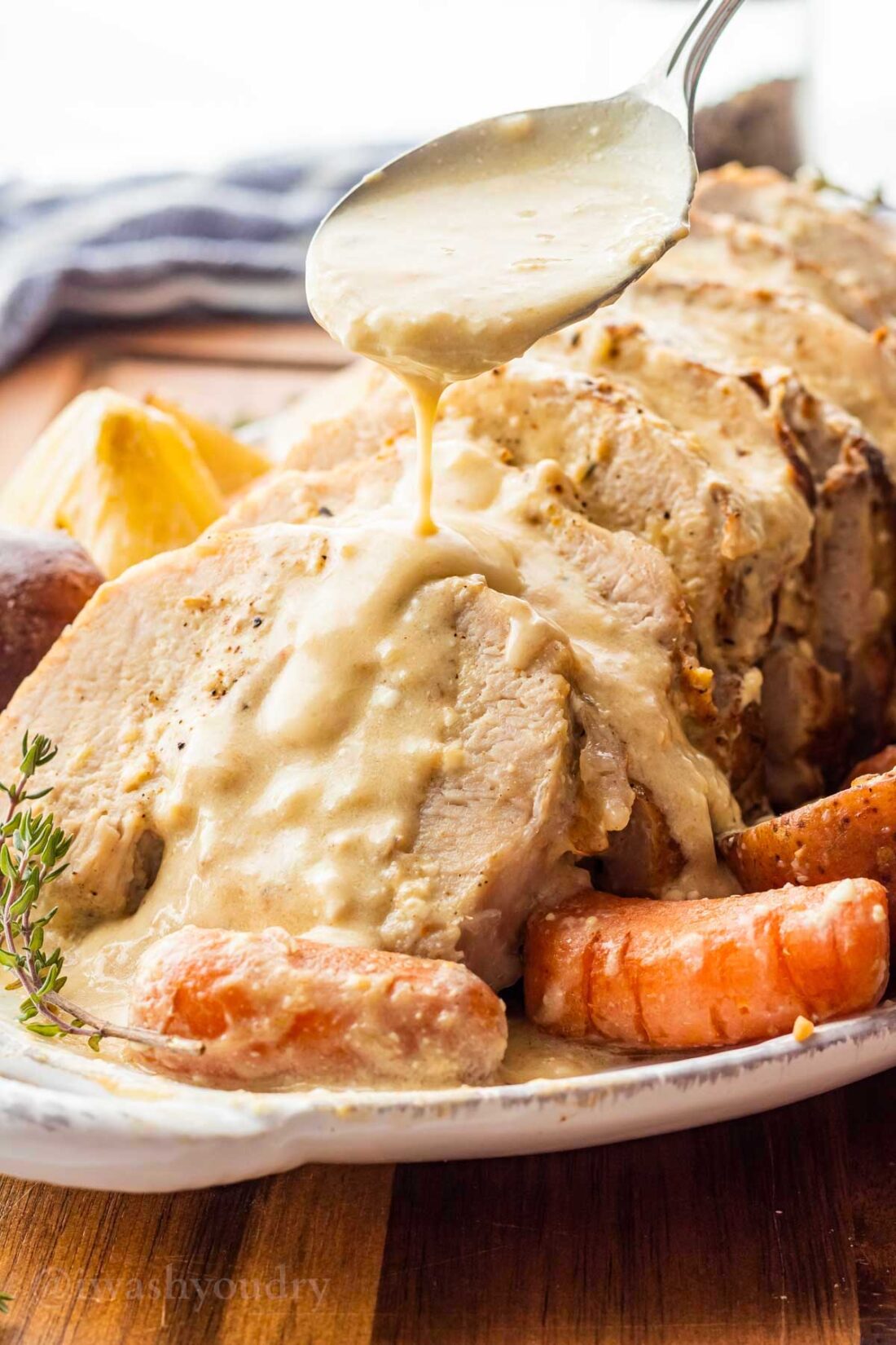 spooning creamy garlic sauce over sliced pork on white plate with carrots.
