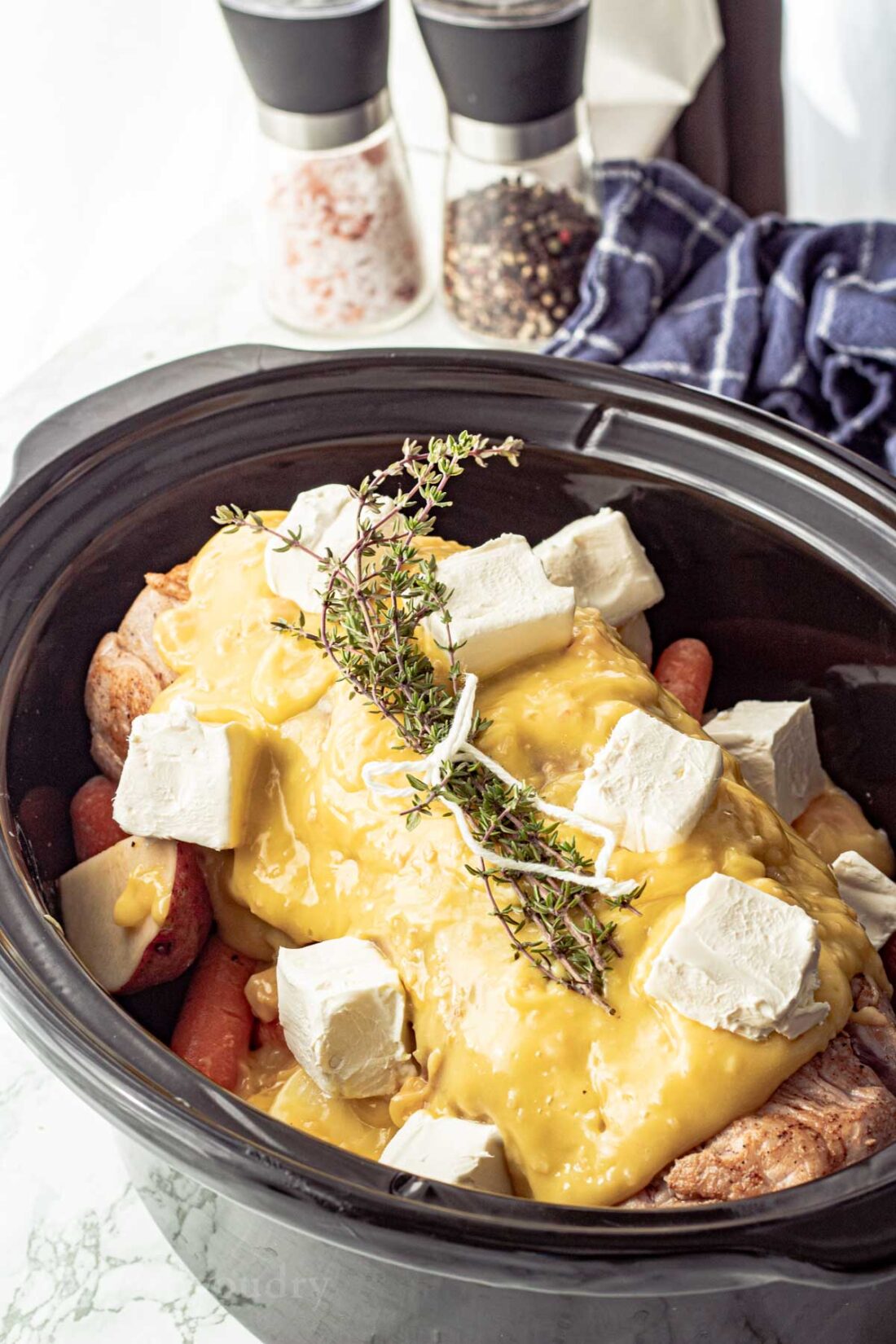 black slow cooker with sauce-covered pork roast and thyme.