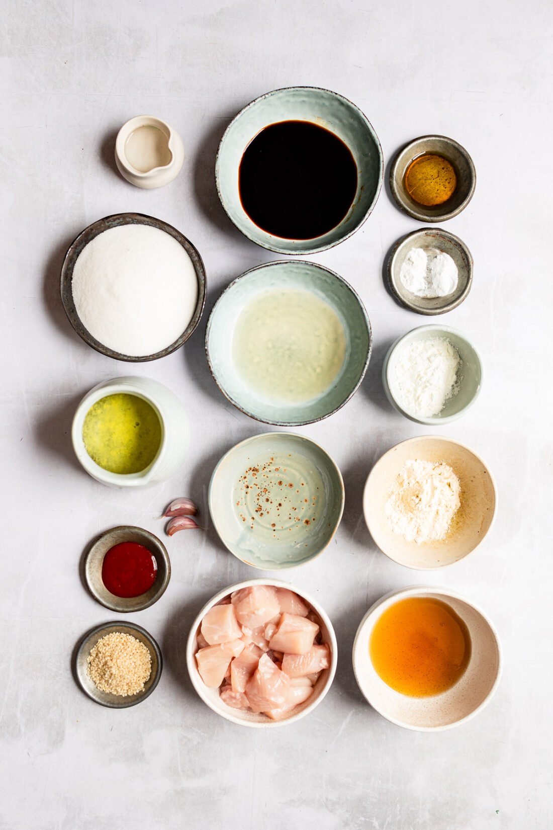 ingredients for sesame chicken recipe laid out in small bowls on white surface.