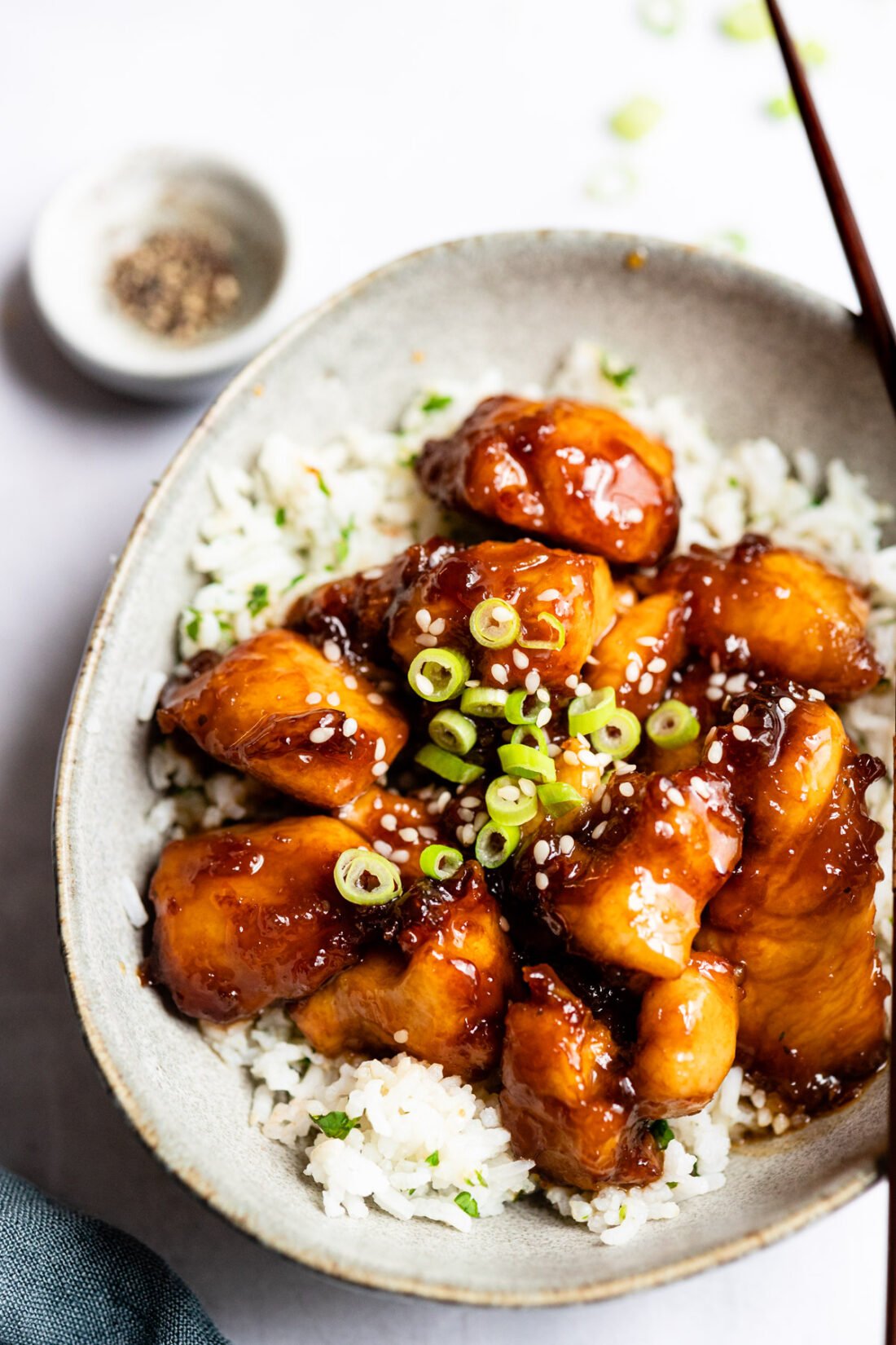 bowl of crispy sesame chicken on top of white rice with chopsticks.