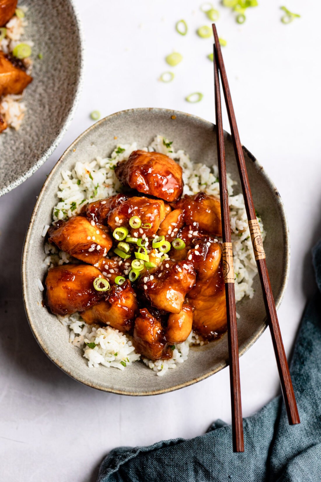 gray bowl with sesame chicken over rice and chopsticks on right side. 