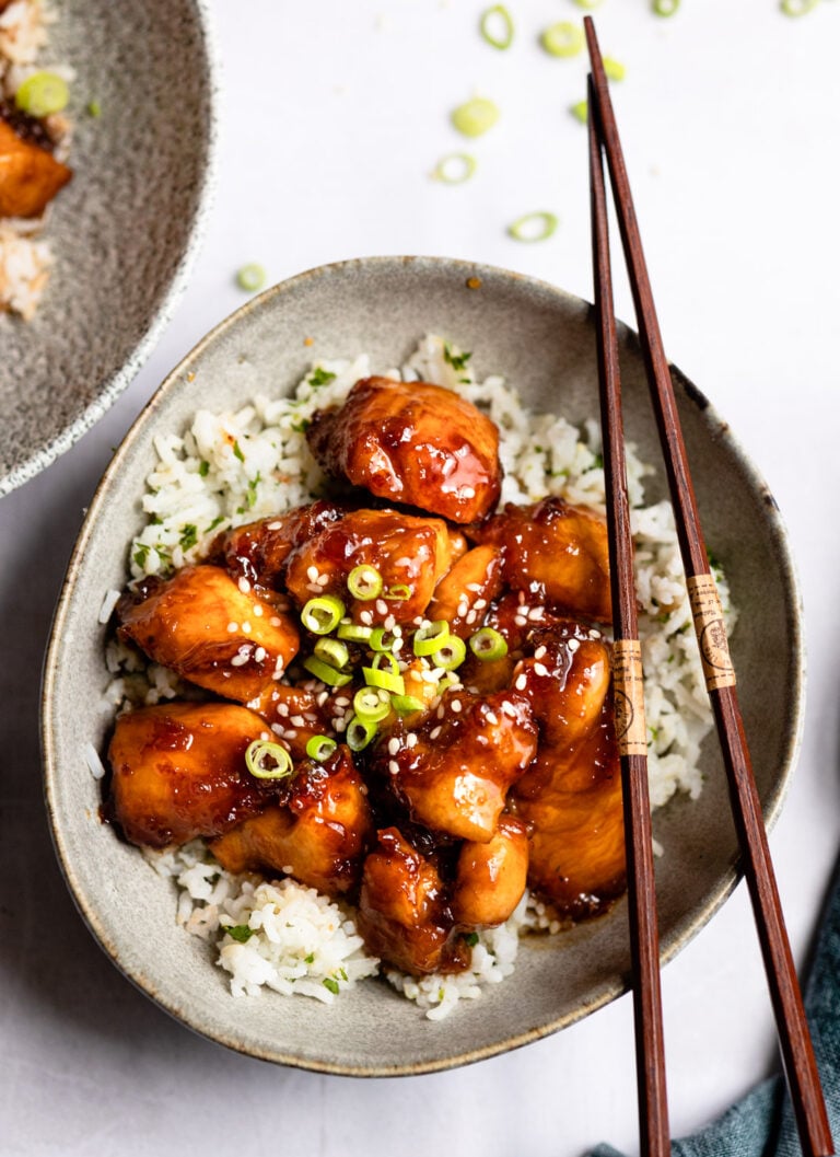 gray bowl with sesame chicken over rice and chopsticks on right side.
