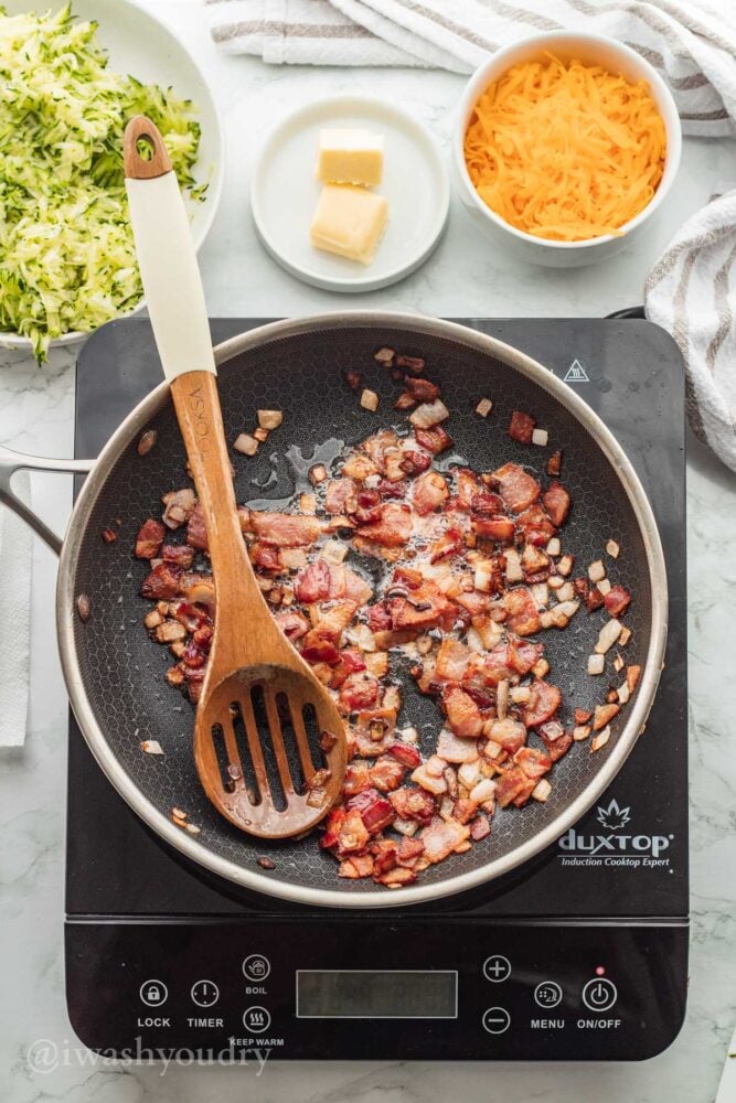 cooked bacon and shallot in skillet with wooden spoon.
