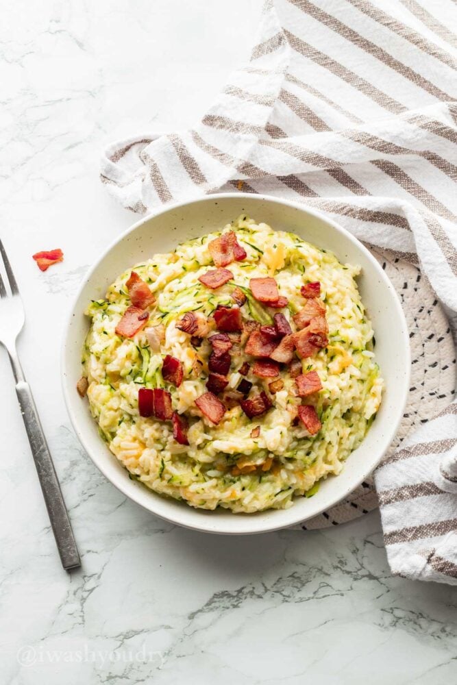 White bowl with shredded zucchini rice and bacon with cheese.