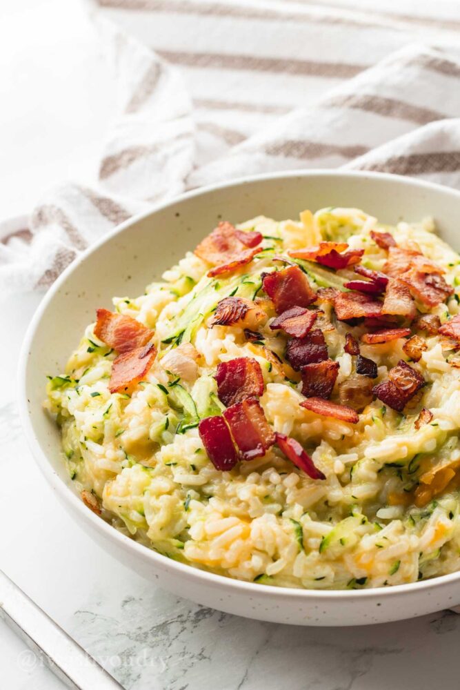 White bowl with rice, cheese and zucchini. Topped with bacon. 
