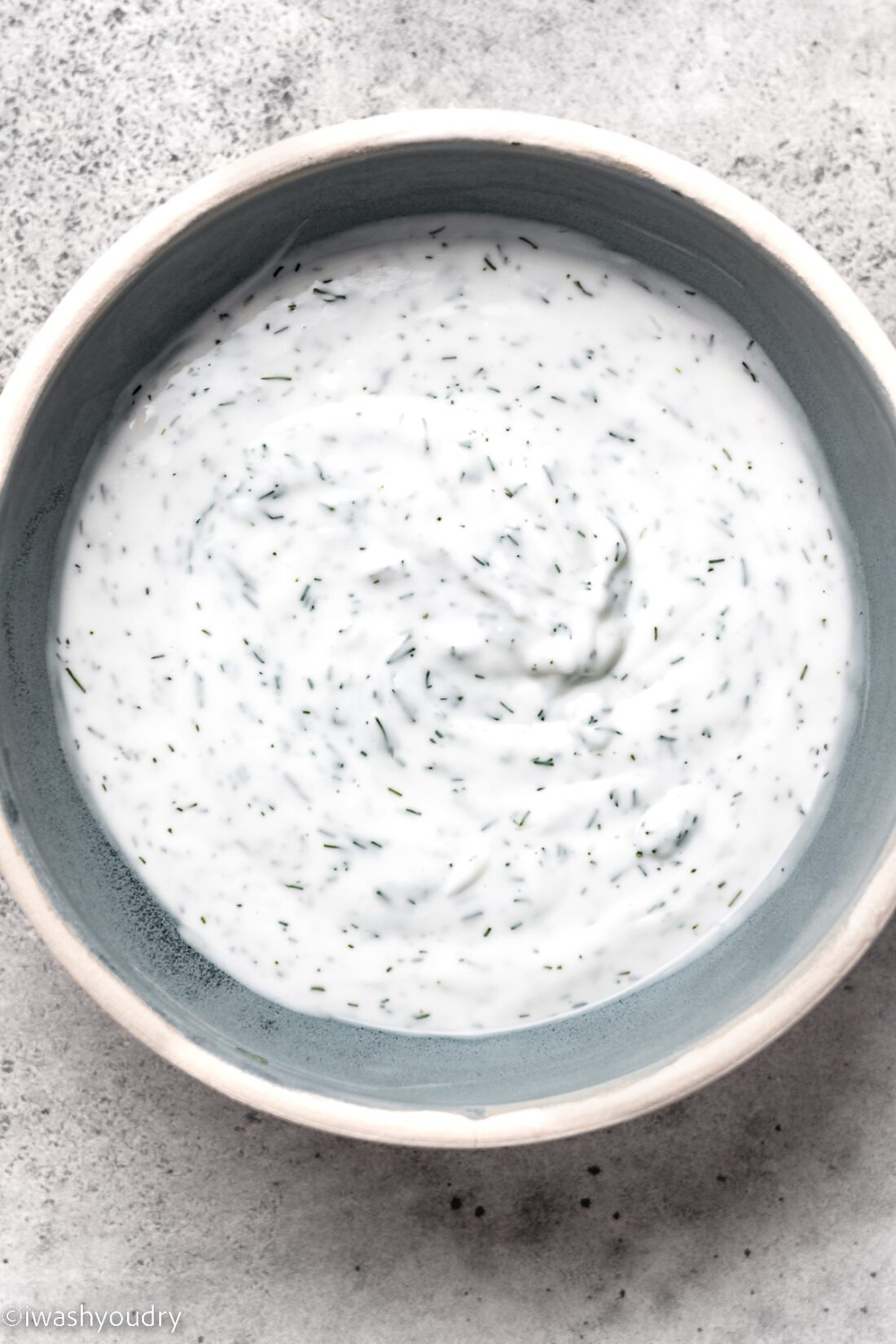 mixed dressing in white bowl with dill weed.