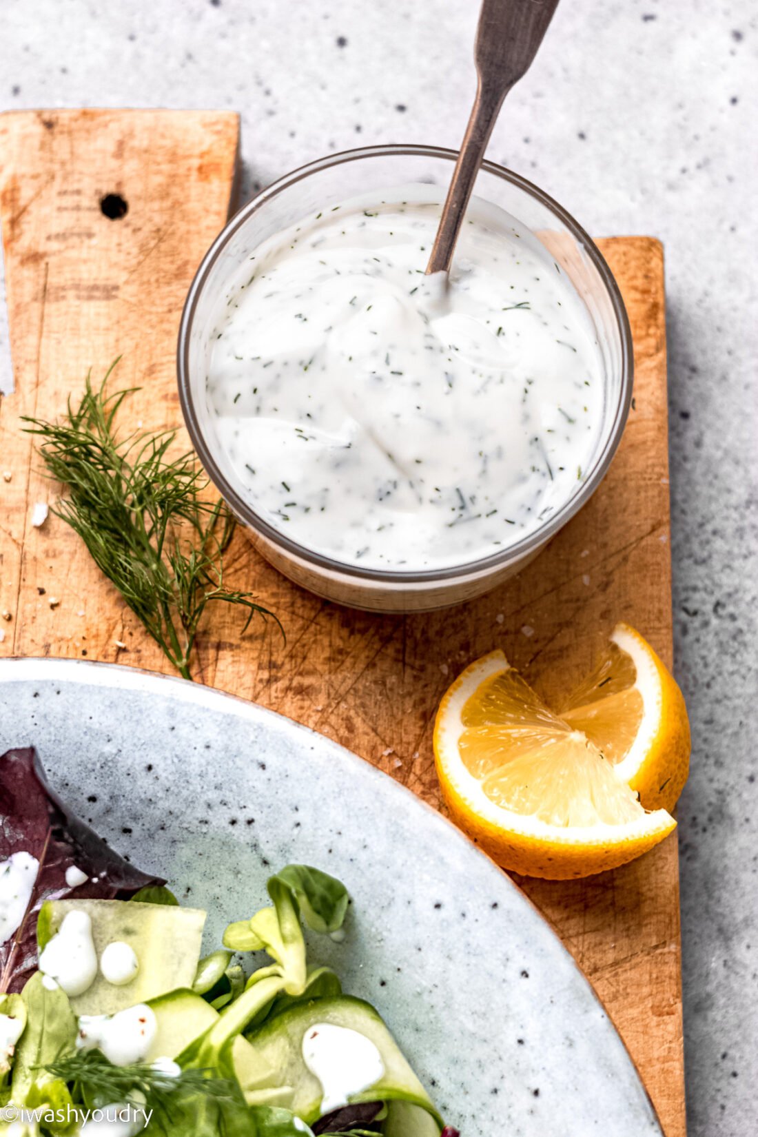 creamy dill dressing on wooden surface with lemon slices.