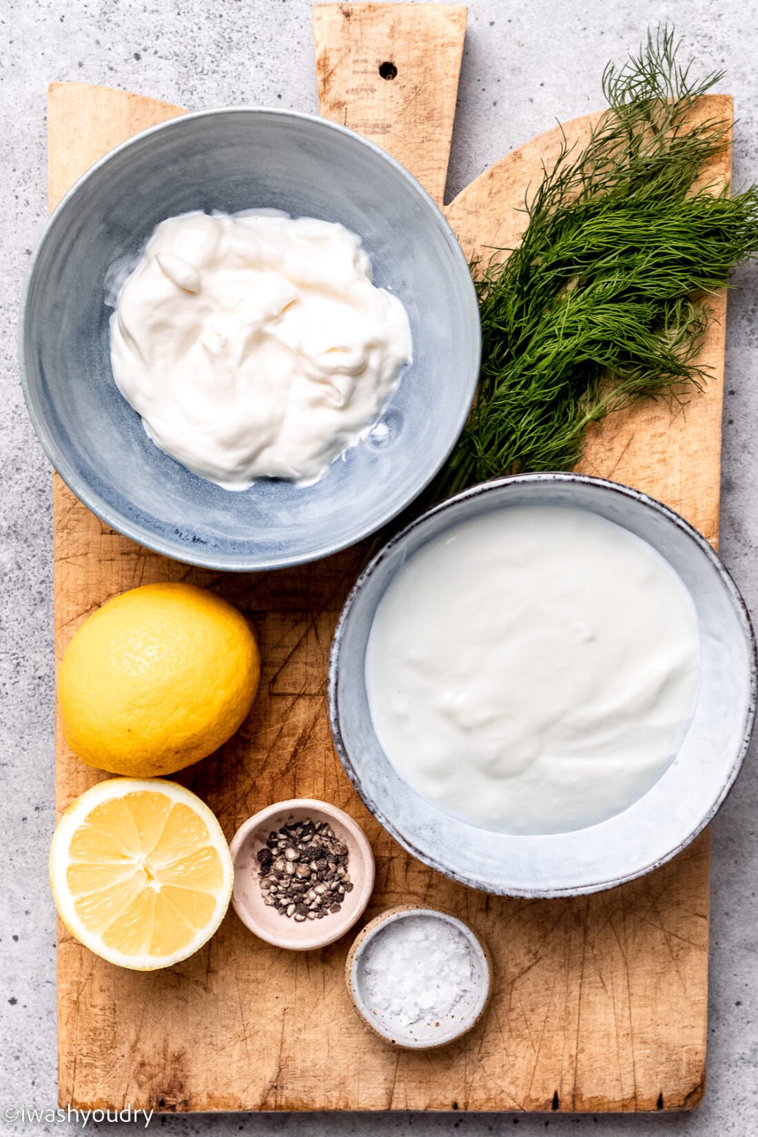 ingredients for creamy dill dressing on wood cutting board with fresh dill and lemons.