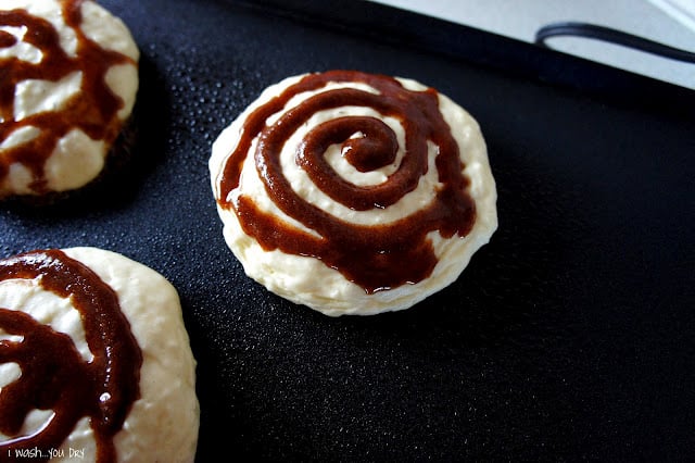 A close up of pancake batter on a skillet with a cinnamon swirl on top. 