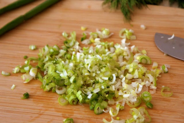 A cutting board with chopped scallions on it next to a knife