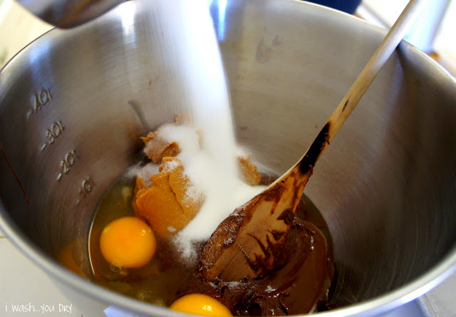 Sugar being added to a mixing bowl with eggs, peanut butter and  Nutella in it.