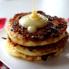 A close up of a display of three pancakes on a plate being topped with a syrup.