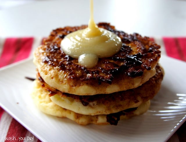 A close up of a display of three pancakes on a plate being topped with a syrup.