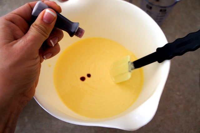 A hand adding drops of food coloring into batter in a bowl