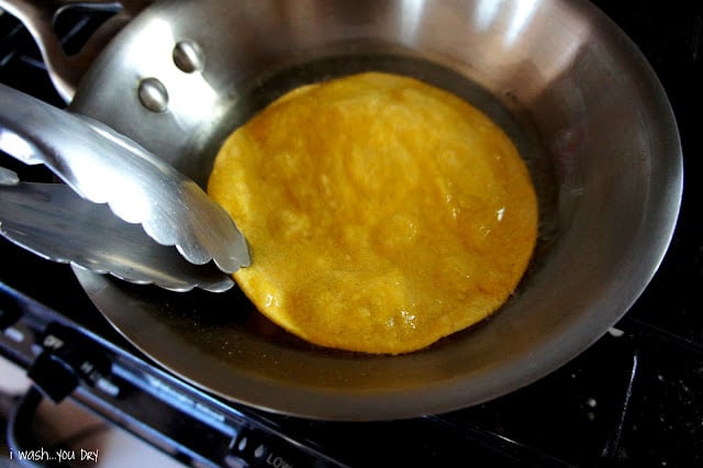 Tongs frying a corn tortilla in hot oil