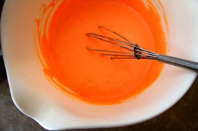 A bowl of orange colored batter with a wire whisk