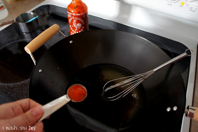 A hand holding a measuring spoon with a red sauce over skillet
