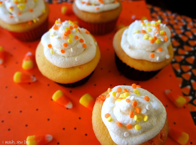 Cupcakes on a table topped with white frosting and yellow, white and orange sprinkles