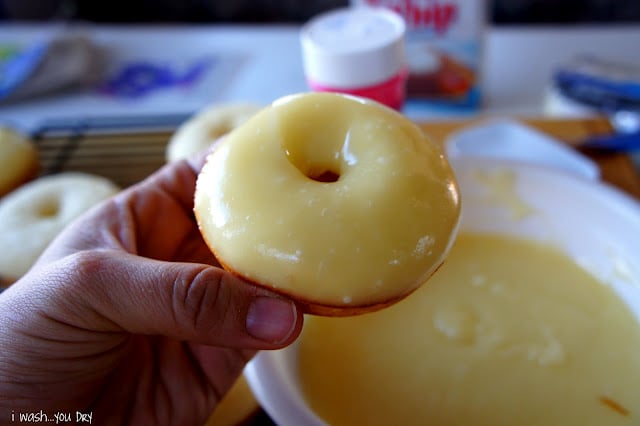 A hand holding a donut freshly dipped in a vanilla glaze topping