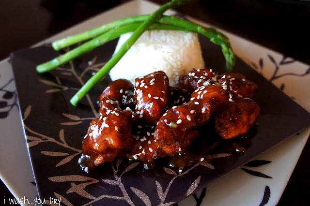 Sesame Chicken displayed on a plate next to a side of rice and asparagus