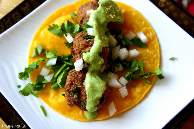 A tortilla topped with meatballs, guacamole and veggies, displayed on a plate