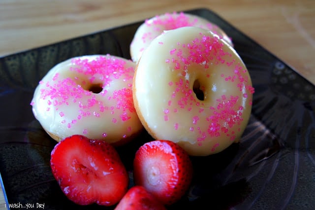 Three donuts displayed on a plate frosted and topped with sprinkles