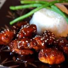 A close up of Sesame Chicken with a side of rice and asparagus