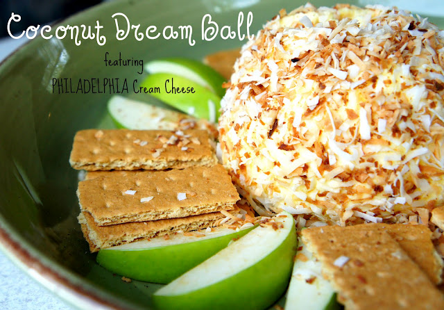 A cream cheese ball displayed on a plate surrounded with apple slices and graham crackers titled, \"Coconut Dream Ball\"