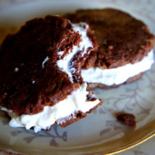 Two cookie sandwiches displayed on a plate; one with a bite taken from it
