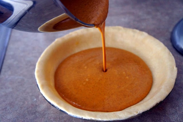 Pumpkin pie batter being poured into a raw pie shell