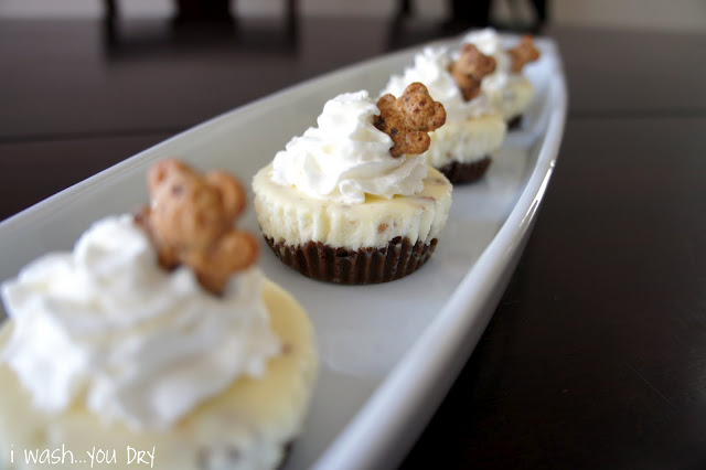 A display of mini cheesecake cupcakes topped with whipped cream and a Teddy Graham