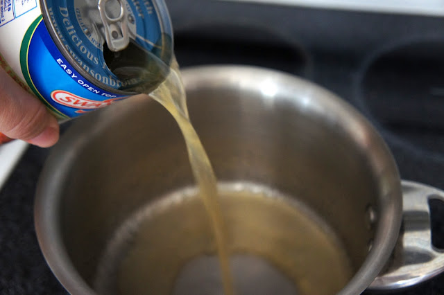A hand pouring a can of chicken broth into a pot