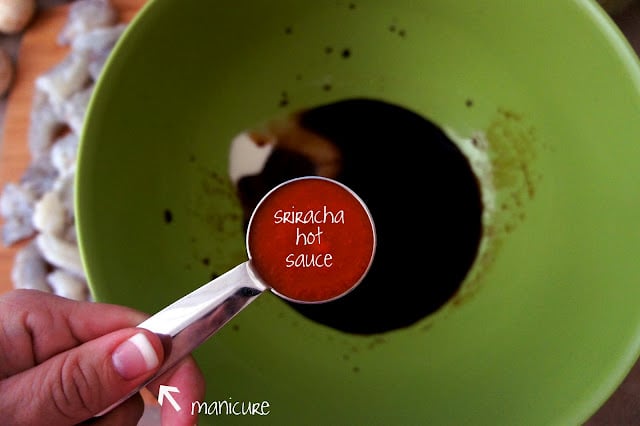 A hand holding a measuring cup of sriracha hot sauce over a bowl of sauce