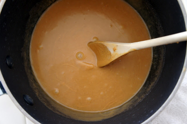 A spoon stirring a pan of melted peanut butter mixture