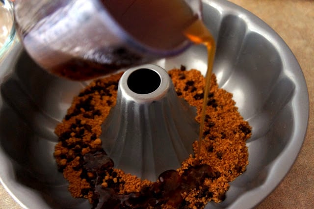 Brown liquid being poured into a fluted pan with other topping ingredients for Chocolate Chip Sticky Bun Ring