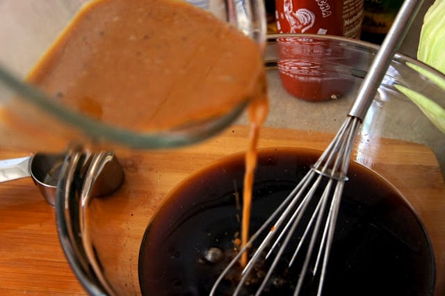 A sauce being poured into a bowl with a dark liquid and a wire whisk
