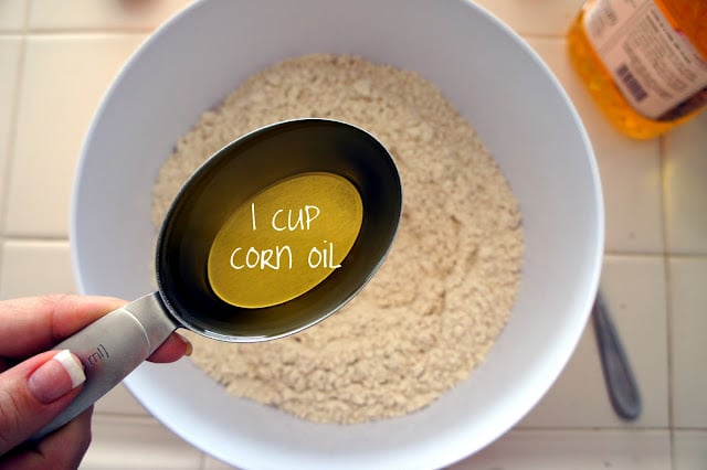 A measuring cup of corn oil above a bowl of powdered mixture