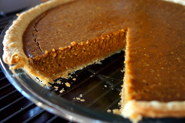 A close up of a pumpkin pie with a slice removed