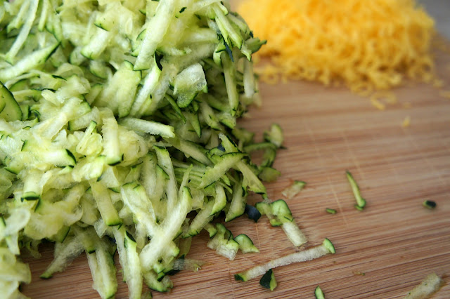 A pile of Shredded Zucchini on a cutting board next to a pile of shredded orange cheese.