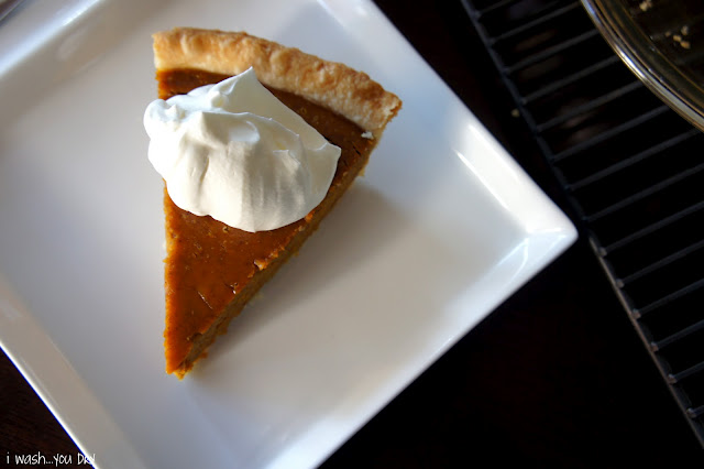 A slice of pumpkin pie on a square plate topped with a dollop of whipped cream