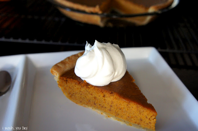 A slice of pumpkin pie on a square plate topped with a dollop of whipped cream