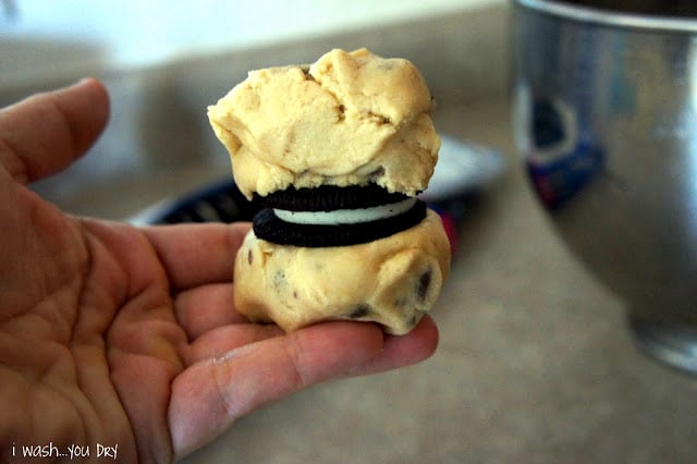 A hand holding an Oreo between two balls of cookie dough