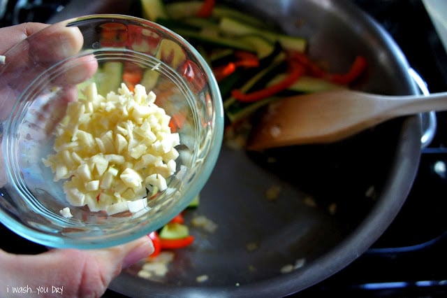 Minced garlic being added to a pan of veggies.