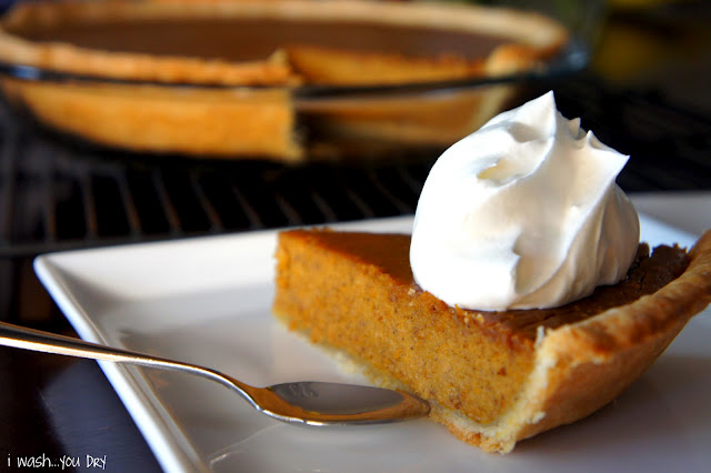 A slice of pumpkin pie on a plate in front of the rest of the pie