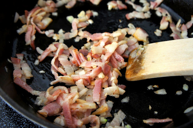 A close up of thin bacon strips cooking in a pan