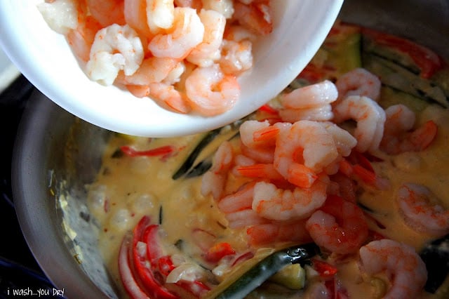 A close up of shrimp being added to a pan of cream sauce and veggies.