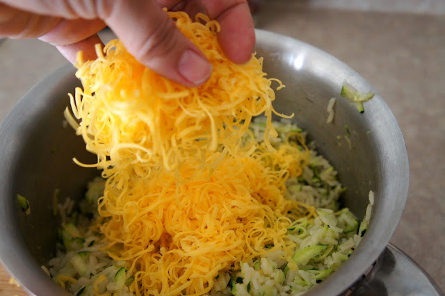 Shredded cheese being added to a pot with zucchini and rice