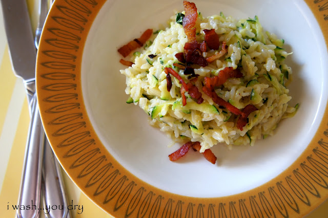 A bowl of cooked rice and zucchini with bacon on top
